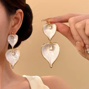 Detail view of retro white enamel heart drop earrings with gold finish worn by model