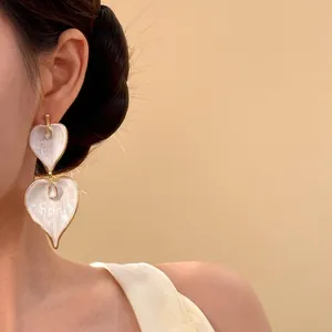 Close-up view of elegant vintage white heart enamel drop earrings worn by a model
