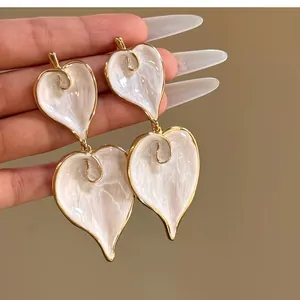 Close-up of vintage white enamel heart earrings featuring elegant gold-toned metallic edges