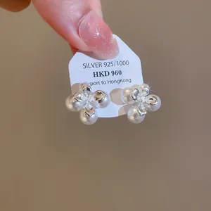 Primo piano di orecchini a lobo a fiore con perle in argento S925 e finitura lucida.