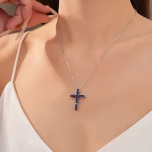 Elegante collar plateado con colgante de cruz de circón azul en el cuello de una modelo