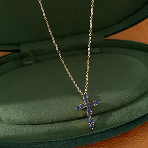 Primer plano de un collar de cruz chapado en oro de 18k con piedras azules en caja verde.