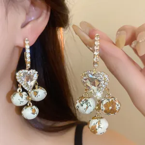 Close-up of crystal heart and floral fabric ball charms on retro French style drop earrings.