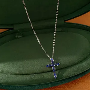 Detalle de un collar con colgante de cruz de circonitas azules en un estuche de terciopelo verde
