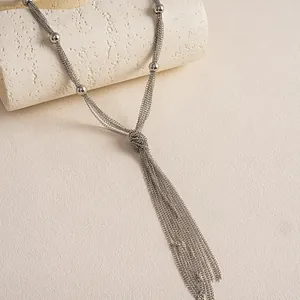 Makroansicht einer mehrlagigen Metallkette mit elegantem Quastenknoten und kleinen Perlen