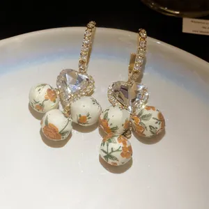 Detail showing French heart-shaped earrings with floral fabric spheres and rhinestones