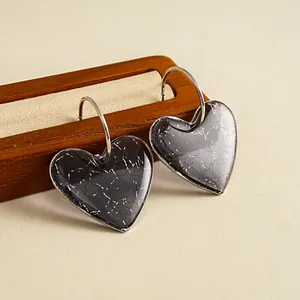 Vue macro de boucles d'oreilles en résine marbrée grise en forme de cœur avec anneaux en C.