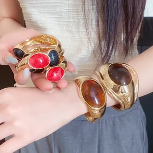 Close-up of vintage oval resin bangles in red, amber, and black on gold bands.