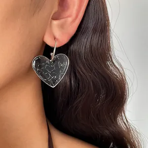 Gros plan d'une boucle d'oreille en résine marbrée sombre portée par un modèle