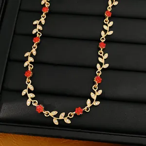Detail view of a gold flower necklace with red crystals and sparkling leaves on black.