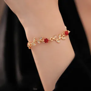 Elegant gold bracelet with red flower and crystal leaf detail shown on the wrist.
