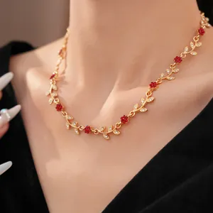 Close-up of an elegant gold necklace featuring red flowers and white crystal leaves