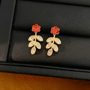 Close-up of elegant gold leaf earrings with red crystal flowers on a black jewelry box.