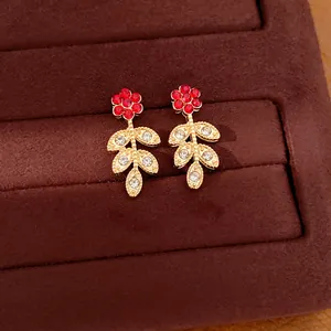 Detailed view of gold earrings with red and clear rhinestones floral leaf design