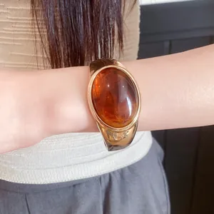 Close-up of a vintage-style gold cuff bracelet featuring a large amber-toned oval resin stone