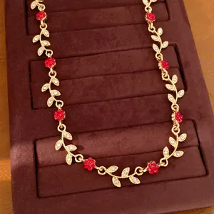 Detailed shot of a delicate gold necklace with red flower and rhinestone leaf motifs