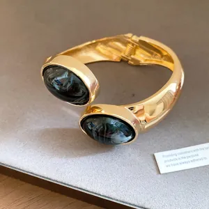 Close-up of retro gold open bangle featuring oval dark marble-textured resin stones.
