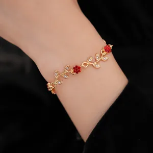 Detailed shot of a delicate gold-toned bracelet with red flowers and rhinestone leaves