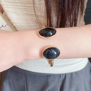 Close-up of a vintage-style gold cuff bracelet with black oval resin marble inserts on wrist.