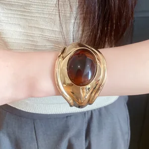 Detail view of a retro oval resin open bangle featuring a polished gold finish and amber stone