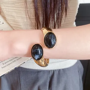 Close-up of golden open bangle featuring black marble-patterned oval resin stones.