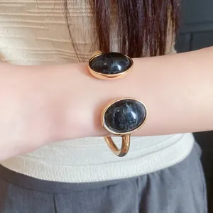 Close-up of a vintage-style gold open cuff bracelet with two oval black resin stones