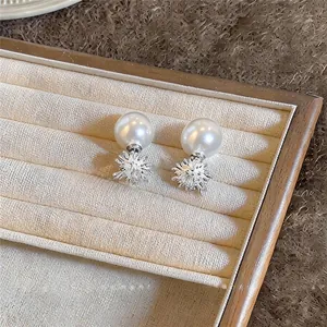 Elegante Franse stijl zirkoon en witte parel oorknopjes op een beige sieradendisplay.
