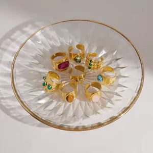 Collection of vintage gold-plated rings with various natural gemstones in a glass dish.