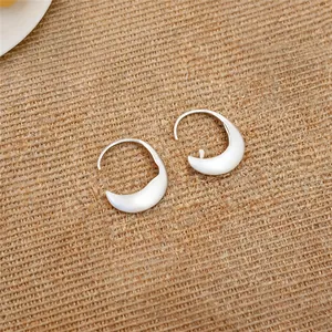 Detailed view of minimalist brushed silver oval hoop earrings on textured burlap background.