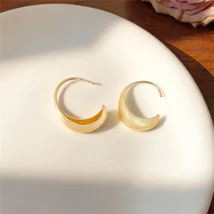 Detail view of minimalist brushed gold oval hoop earrings displayed on white ceramic plate