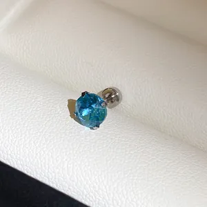 Detailopname van een roestvrijstalen oorknopje met een briljante ronde blauwe edelsteen.