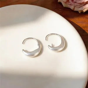 Elegant silver oval crescent hoop earrings with a brushed matte finish on a ceramic plate