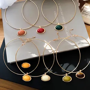Elegant gold chokers with colorful oval resin pendants in a minimalist lifestyle setting