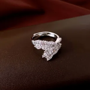 Primo piano di un anello aperto in argento con zirconi geometrici su pelle marrone.