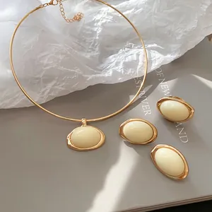 Detailansicht eines goldenen Schmucksets mit ovalen cremefarbenen Harzsteinen auf grau.