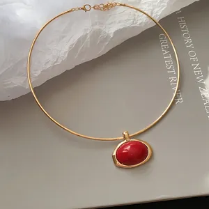 Nahaufnahme eines goldenen Chokers mit elegantem roten ovalen Harzanhänger auf Buch.
