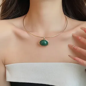Nahaufnahme eines eleganten Gold-Chokers mit einem grünen ovalen Harzanhänger am Model.