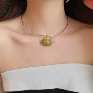 Detailaufnahme eines minimalistischen goldenen Halsreifs mit grünem Harzanhänger
