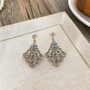 Close-up of elegant gold earrings with water-drop diamond design on a textured board.