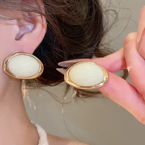 Nahaufnahme eleganter ovaler Harzohrringe mit goldfarbenem Rahmen am Ohr des Models