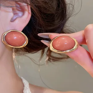 Detailansicht eleganter ovaler Harzohrringe mit goldfarbenem Metallrahmen am Ohr