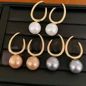 Gouden creolen met witte, perzik en grijze parels op een zwarte sieraden display
