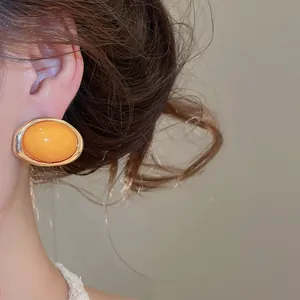 Nahaufnahme vintage orange ovaler Harzohrring mit goldfarbenem Metallrand