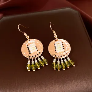 Detailaufnahme von Vintage-Goldohrringen mit faltigen Scheiben und grünen Perlenquasten