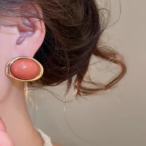 Detailansicht eleganter ovaler korallenroter Harzohrringe mit goldenem Metallrahmen am Modell