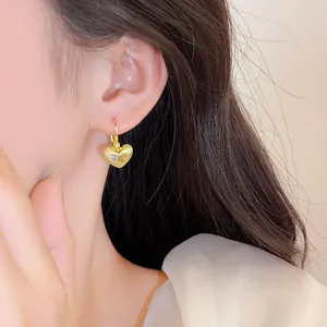 Close-up van een goud vergulde hart oorbellen met zirkonia op het oor van een model