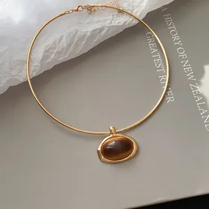 Eleganter goldener Halsreif mit ovalem Harzanhänger auf schickem Buchhintergrund