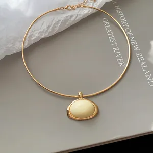 Detailansicht eines vergoldeten Chokers mit einem eleganten cremefarbenen Harzanhänger
