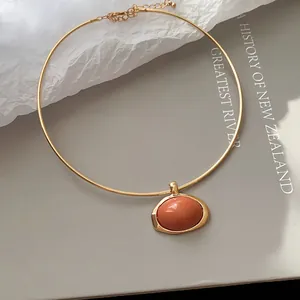 Nahaufnahme eines goldenen Halsreifs mit einem ovalen Harzanhänger in Terrakotta