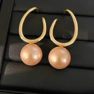 Macro view of geometric gold hook earrings featuring large round salmon pearls on tray